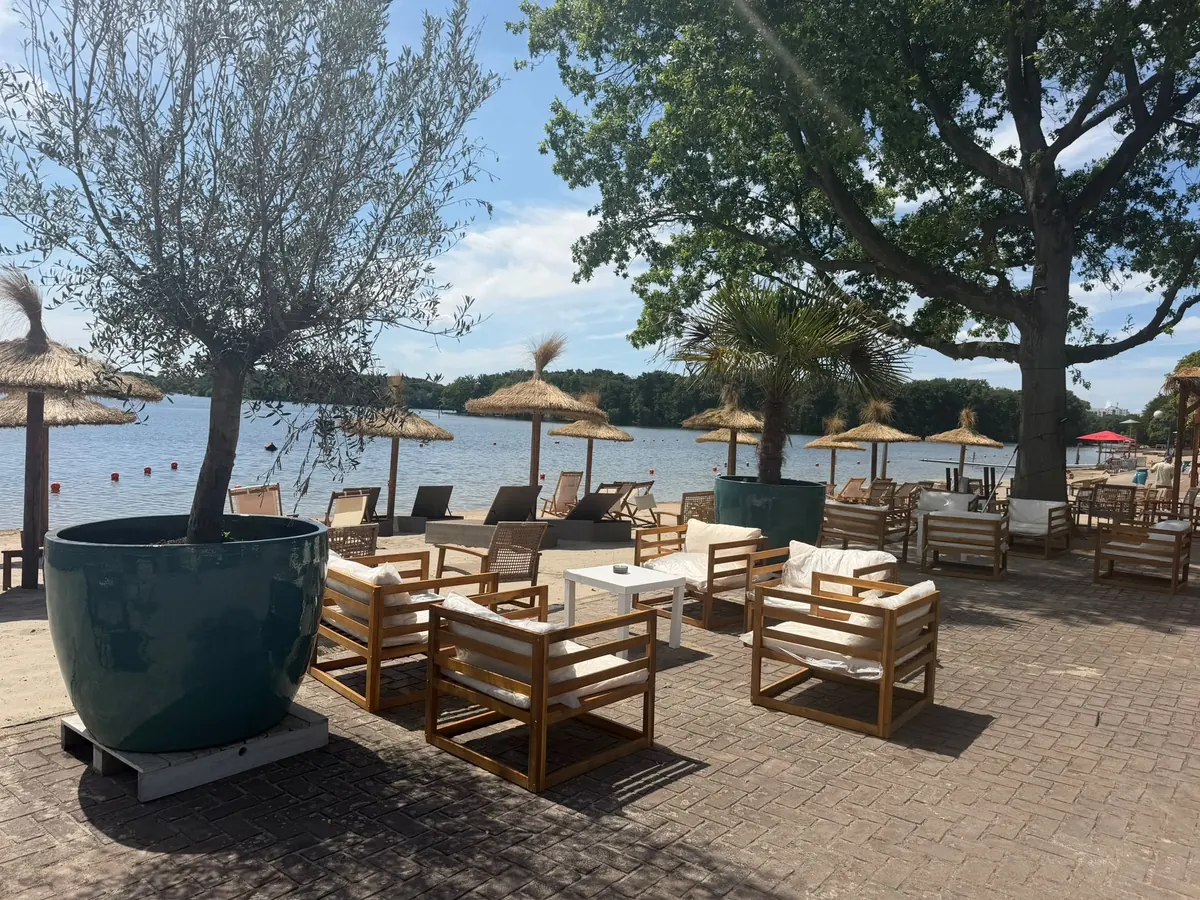 Loungeecke mit Olivenbaum und Strohschirmen am See