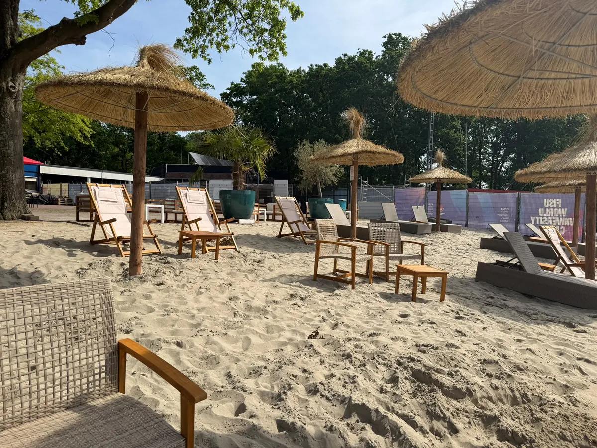 Korbsessel und Liegestühle unter Strohschirmen im Sand